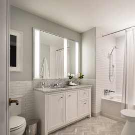 Luxuriate in master baths featuring white natural stone vanity, Kohler fixtures and accessories in polished chrome, and natural stone tile floor in white herringbone tile.