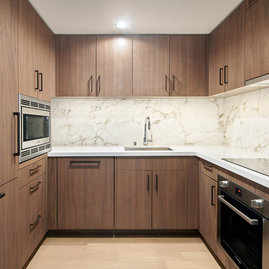 White quartz counters and Calacutta marble backsplash, soft-close wood cabinetry, stainless steel sink and premium stainless steel appliances with integrated wood paneling.