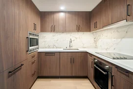 White quartz counters and Calacutta marble backsplash, soft-close wood cabinetry, stainless steel sink and premium stainless steel appliances with integrated wood paneling.