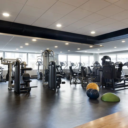 A state-of-the art Health and Fitness Center features cardio and strength equipment and lots of natural light streaming through a wall of windows.