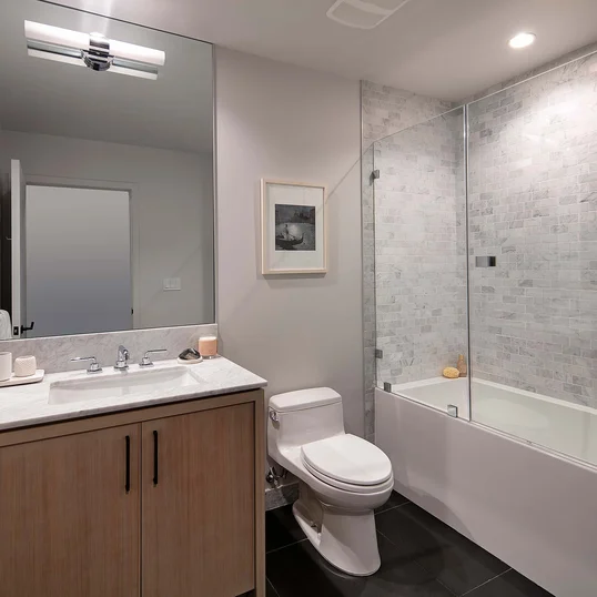 Luxe baths include a custom grey oak bathroom vanity with marble counters, frameless glass-enclosed showers with marble tile wet walls and oversized porcelain tile flooring.